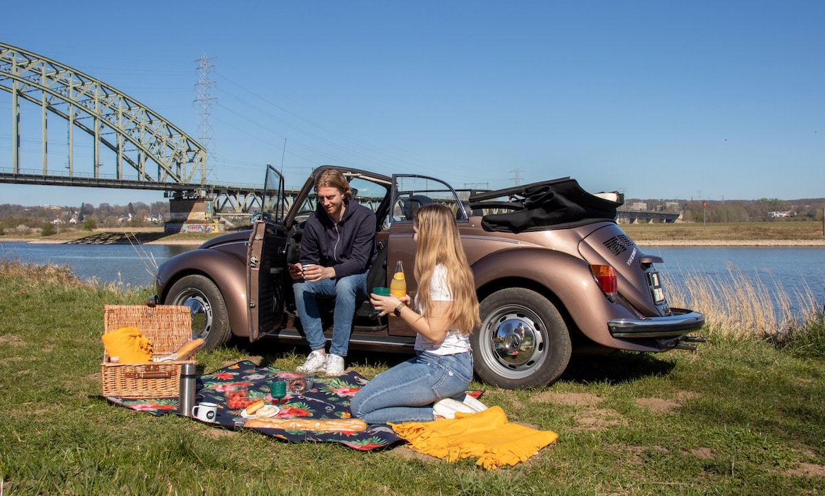 Man en Vrouw picknicken naast een Oude Volkswagen Kever