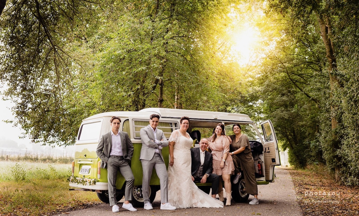 Drie mannen en drie vrouwen voor een groene Volkswagen bus bij een bruiloft