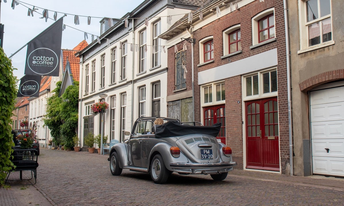 Grijze Volkswagen Kever met het dak open rijdend door Doesburg